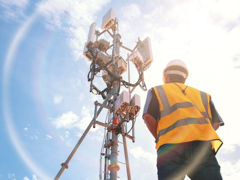 An engineer stands next to a telecommunications tower while working in the field